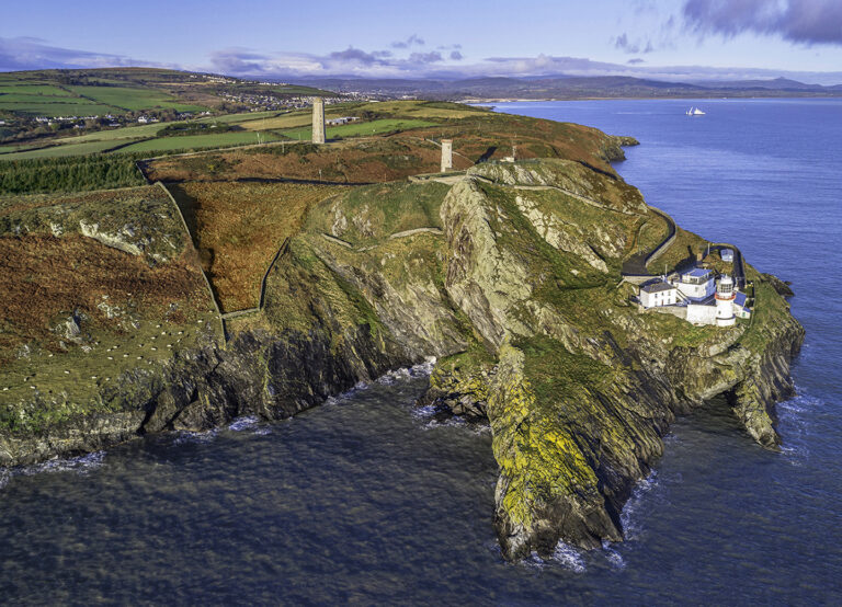 Aerial view of Wicklow Dunbur head featuring the current lighthouse nearest the coastline and the old Wicklow Head Lighthouse, a stone round tower behind.