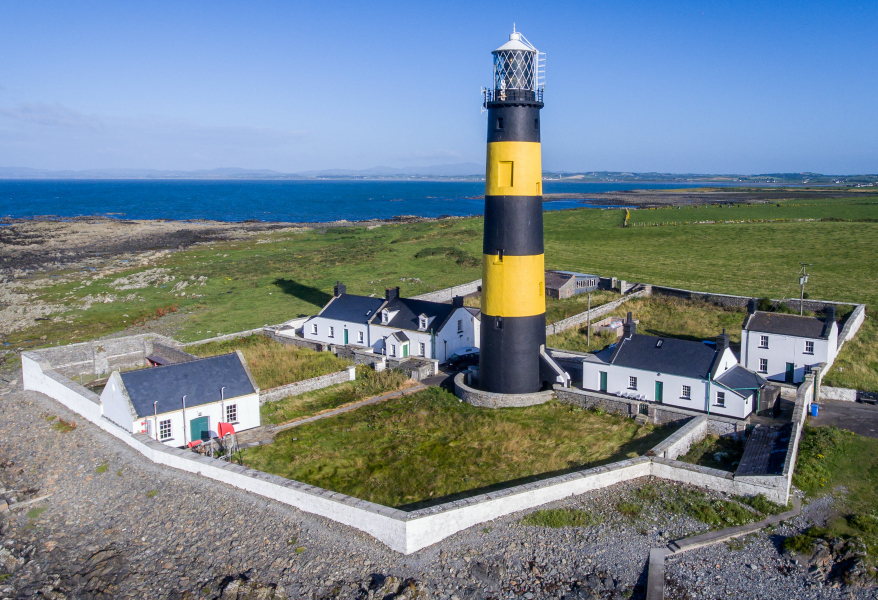 Aerial view of the striking John's Point in County Down, a tall lighthouse with navy and yellow stripes. Several houses are in the compound, two of which are available to rent